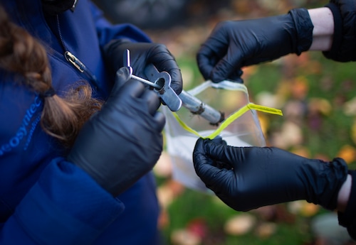 Two people gather soil samples from a grassy parking strip.