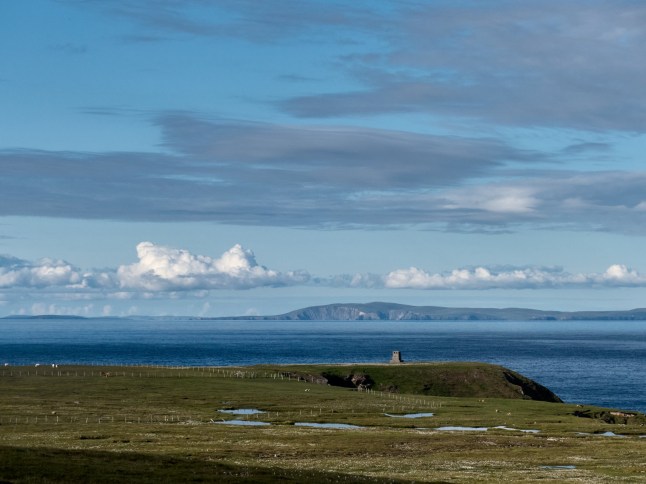 View over Foula and the monument towards Mainland Shetland. Foula is located in the Shetland archipelago of Scotland and one of the United Kingdom's most remote permanently inhabited islands. Foula lies 28 kilometres west of Walls in Shetland. 38 people live on the island.