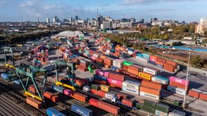 An aerial view of the Freightliner Rail Terminal at Landor Street in Birmingham with shipping containers loading onto freight trains and cityscape skyline in the background.