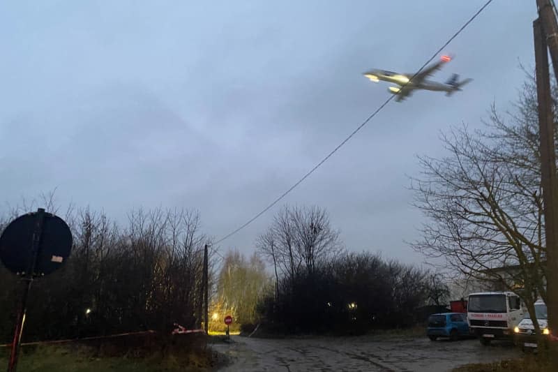An airplane flies over the cordoned-off crash site. Investigators in Lithuania assume that the data from the flight data recorder and the voice recorder of the crashed cargo plane from Germany can be read out in the near future. Alexander Welscher/dpa