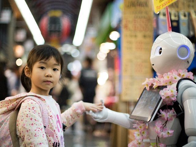 Young girl puts her hand into a robot's.