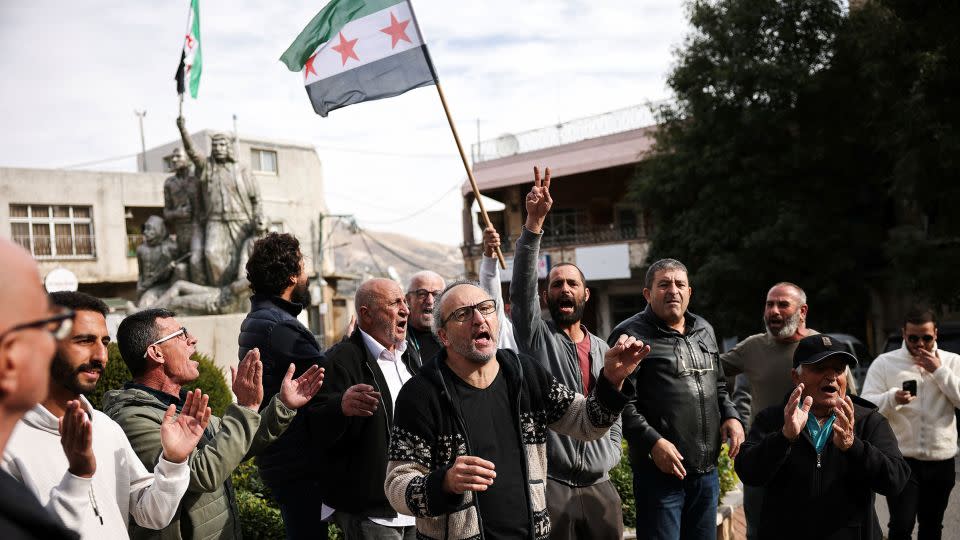 A person holds up a Syrian opposition flag in a Druze village in the Israeli-occupied Golan Heights, on December 8, 2024, as men celebrate the fall of Assad's regime. - Stoyan Nenov/Reuters