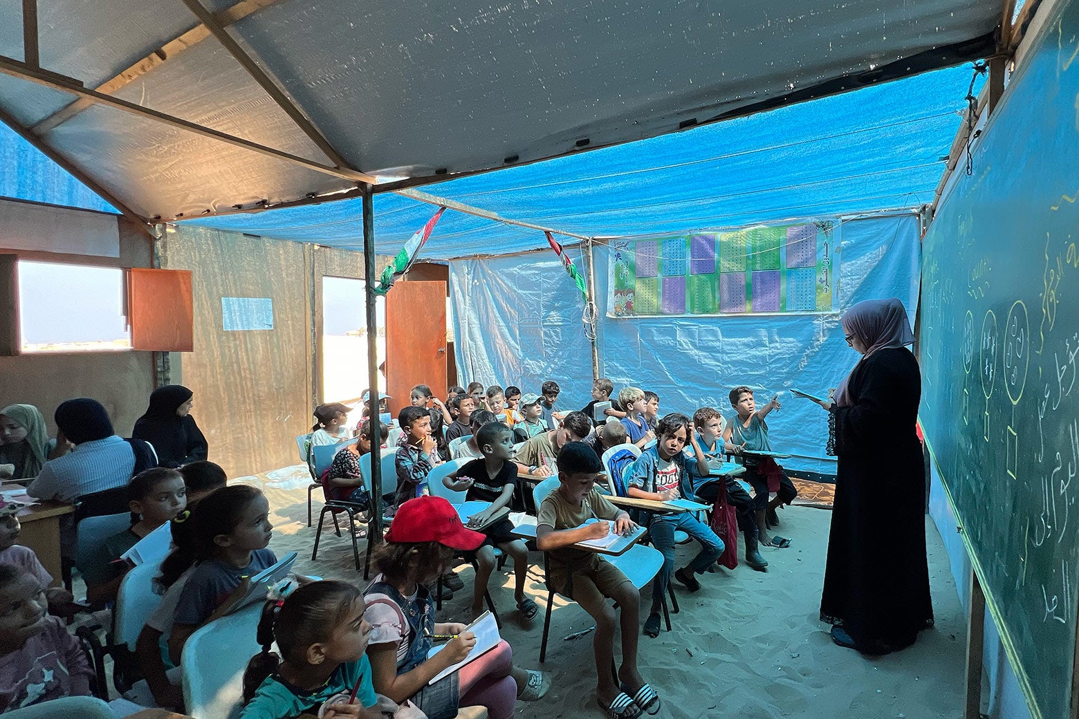 The blue-tarp classroom's view from the front of the children engaged in the lesson.