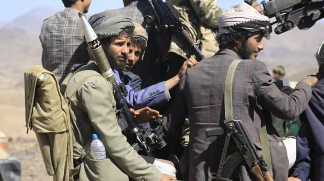 Three Houthi fighters, holding weapons and looking off into the distance.