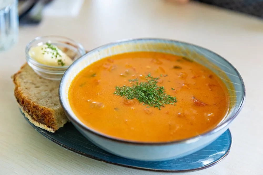 A bowl of creamy Icelandic langoustine soup garnished with herbs, served with crusty bread and butter on the side
