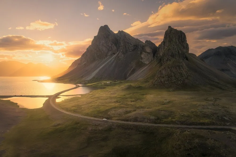The dramatic peaks of Vestrahorn at Stokksnes, bathed in golden sunset light, with a winding coastal road leading to the sea