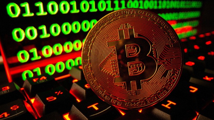 Bitcoin cryptocurrency representation pictured on a keyboard in front of binary code