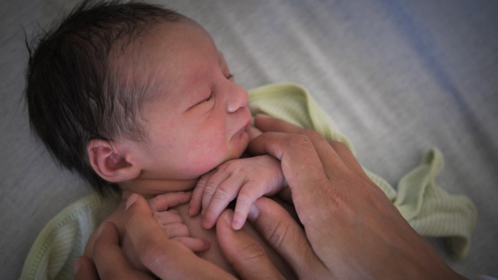 A newborn baby is gently cradled by a mother's hands in a hospital.