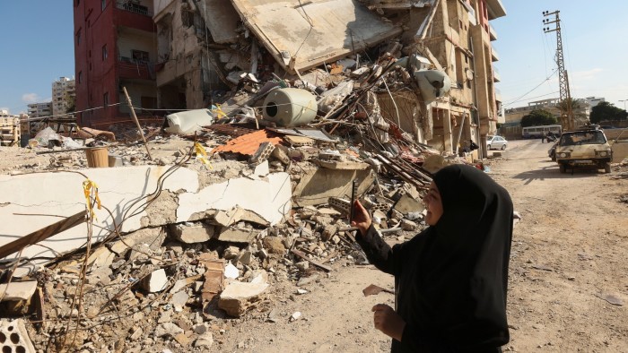 A woman in Tyre, southern Lebanon, uses her mobile phone among the rubble of a destroyed building after a ceasefire between Israel and Hezbollah