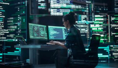 Female Developer Thinking and Typing on Computer, Surrounded by Big Screens Showing Coding Language (Shutterstock)