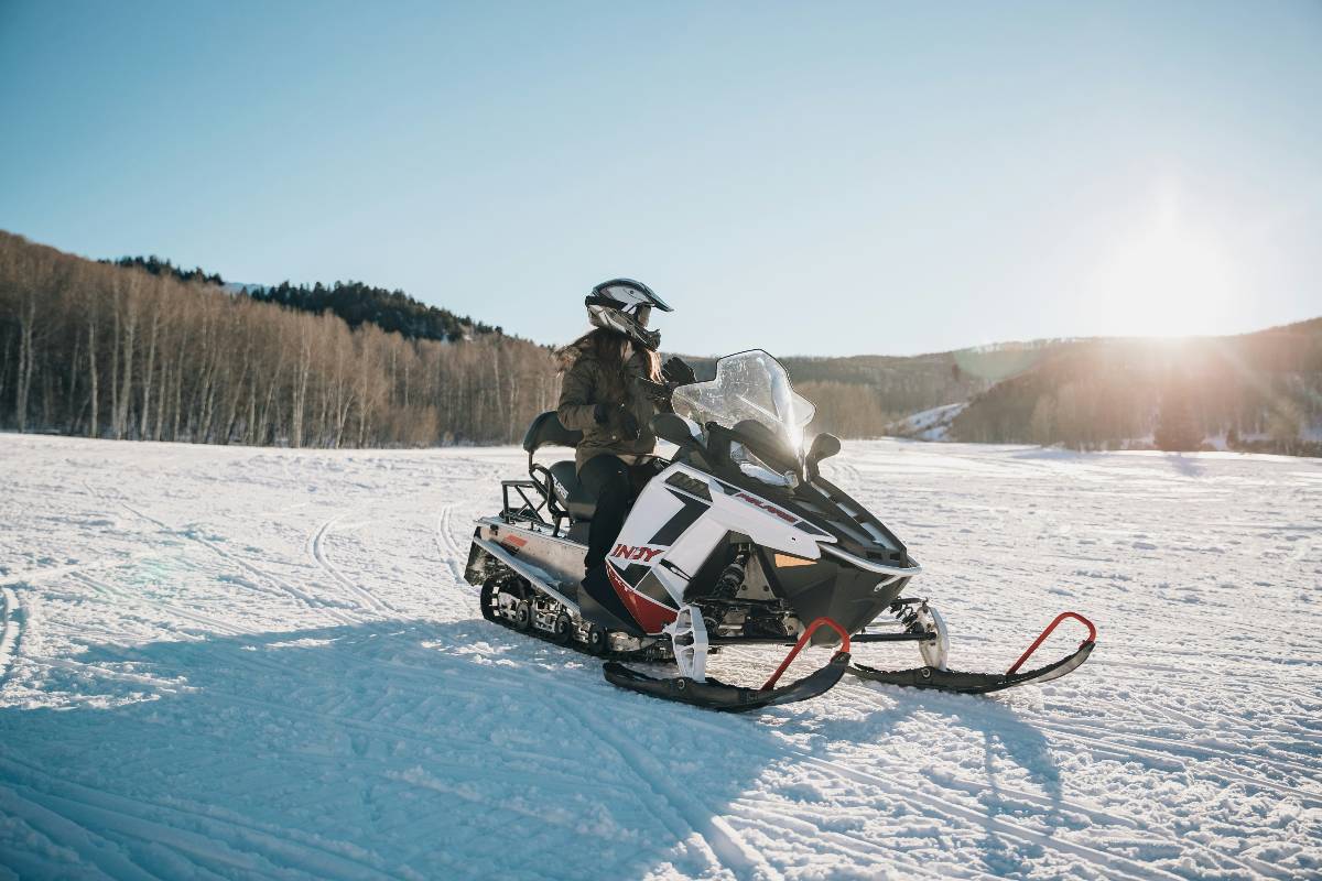 A person on a snowmobile surrounded by snow next to a forest