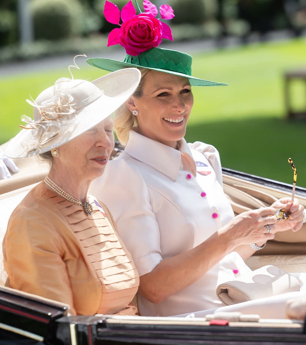 Zara Tindall smiling wearing a white suit dress sitting next to her mother on a royal carriage.
