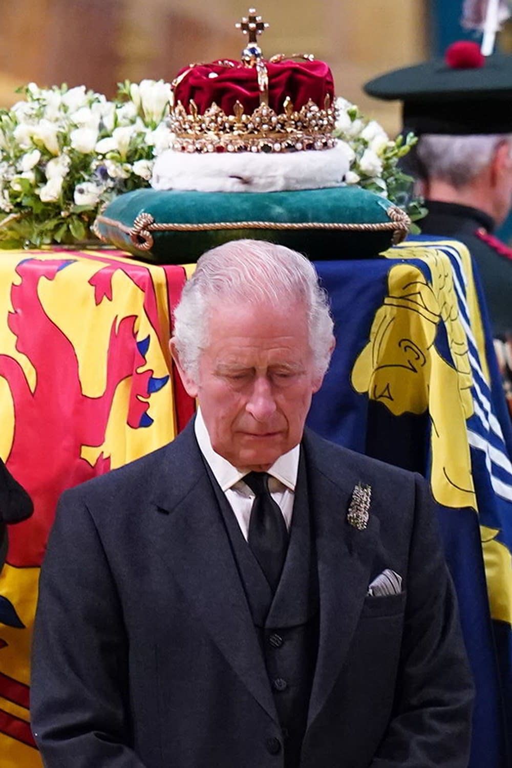 King Charles looking sad with a crown above his head on top of Queen Elizabeth's coffin.