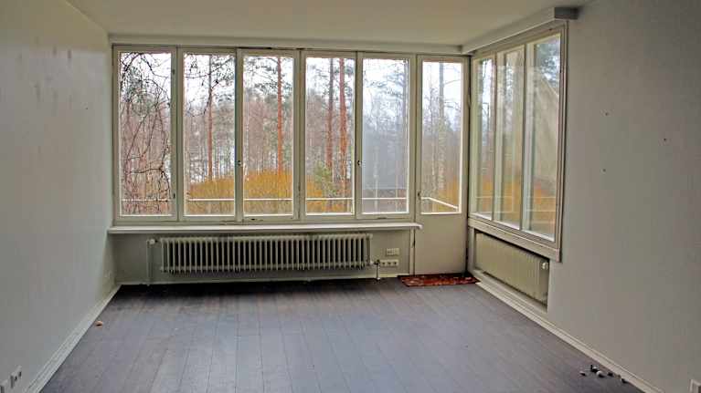 Valoisa tyhjä huone, jossa on suuret ikkunat ja näkymä ulos puiden ja luonnon keskelle.
