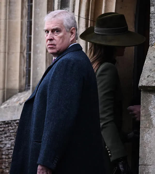 Prince Andrew looks directly back at the camera in a long coat while Kate Middleton walks inside in a green hat and coat