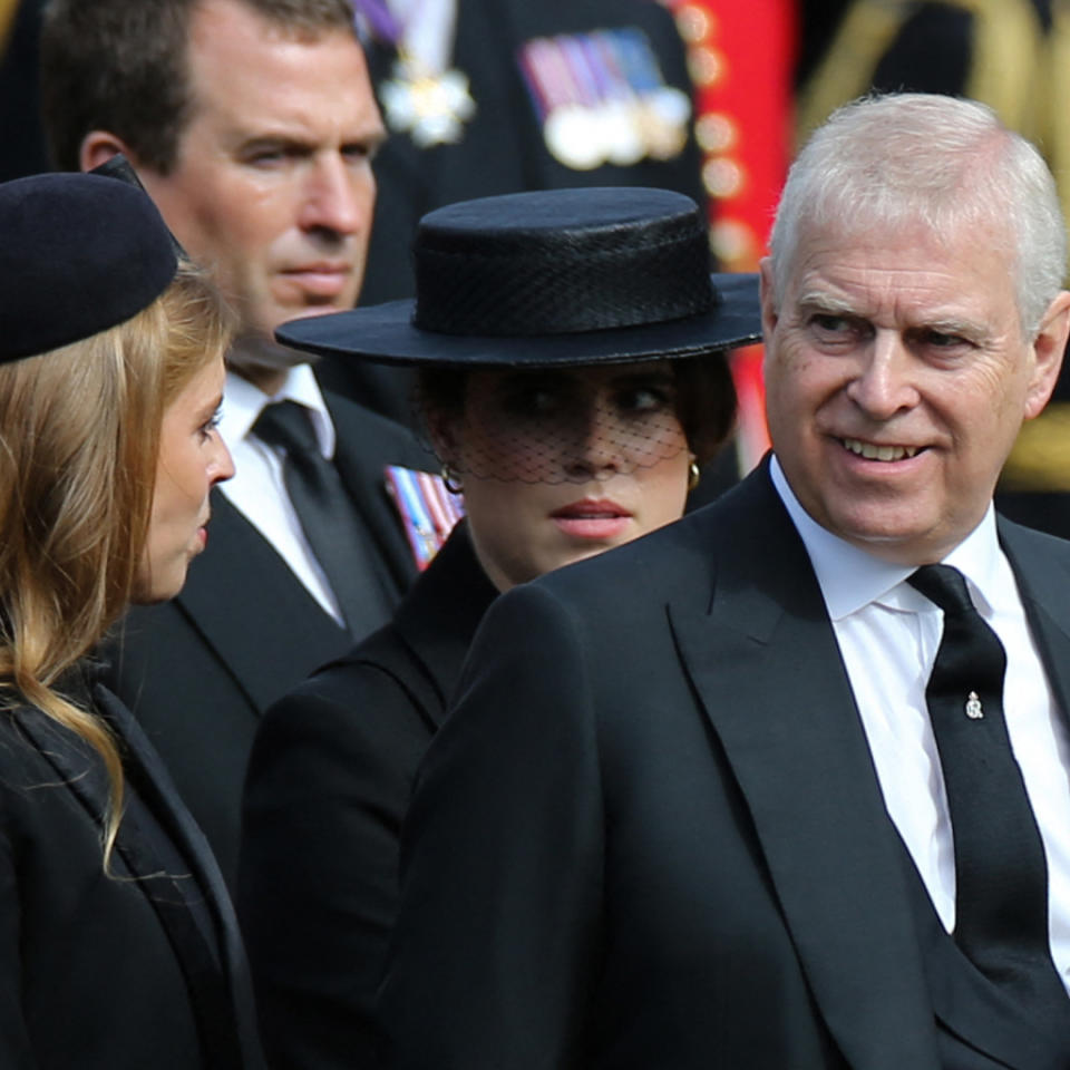  Princess Beatrice and Princess Eugenie wearing black hats and coats standing next to Prince Andrew who is smiling and wearing a black suit with military medals. 