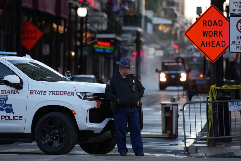 A law enforcement officer stands near a police vehicle and a barricade on Canal and Bourbon streets in New Orleans