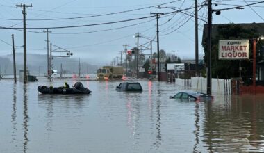 Submerged cars float in the forefront as a National Guard vehicle approaches a flooded railroad track in Monterey County California