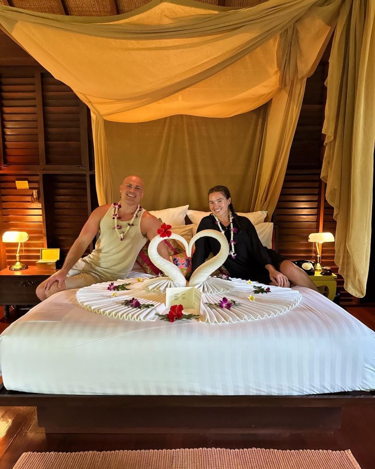 Couple sitting on a bed decorated with towel swans and flowers.