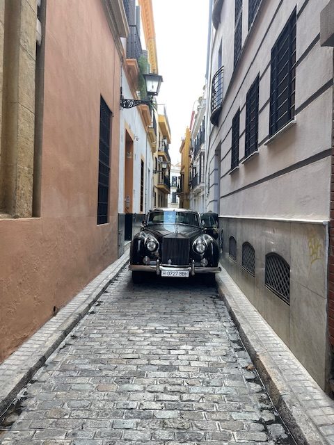 A car squeezes between two buildings on a very narrow street