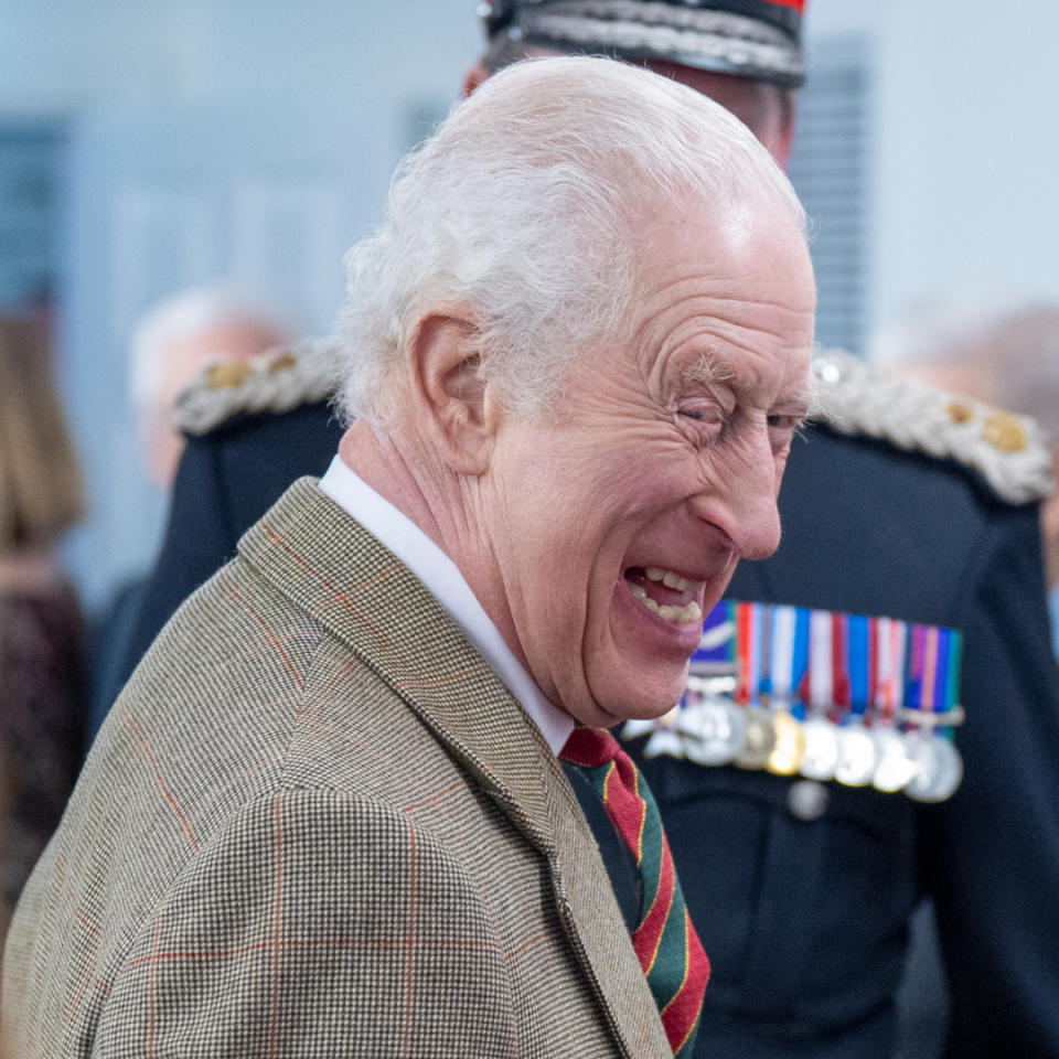 King Charles wearing a tan blazer and striped tie turning to the side and laughing surrounded by a group of people .