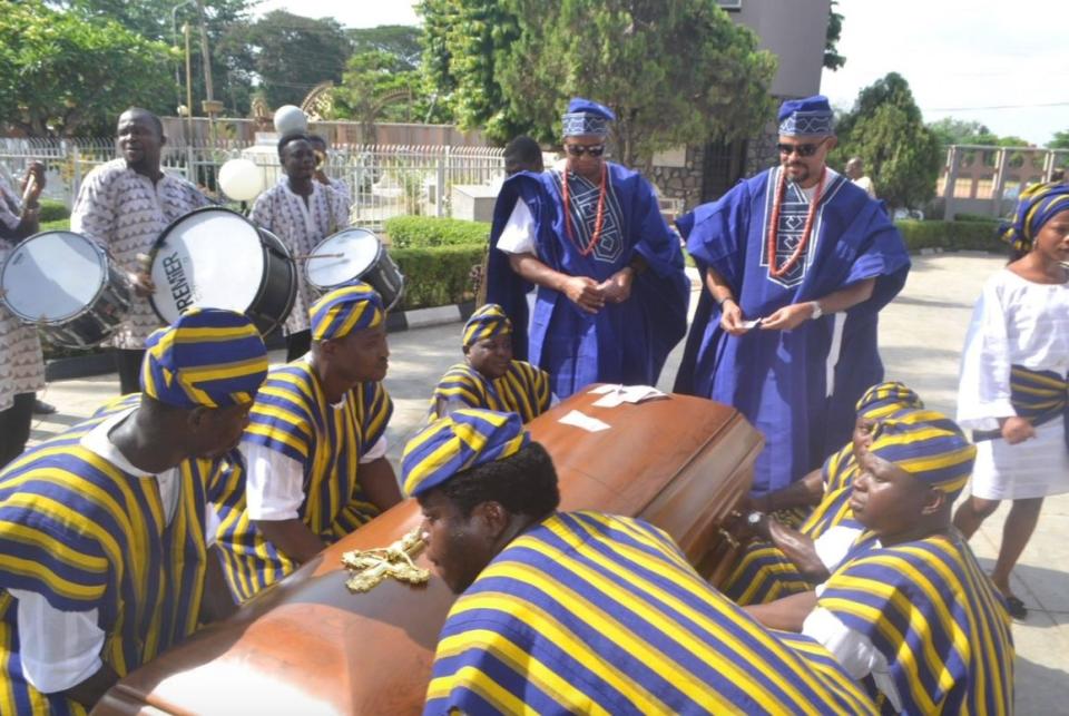 Just before the author's father's funeral, Mike, the author's husband (left), and Femi, the author's brother, put money on the coffin, a sign of respect