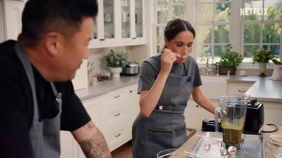 Meghan Markle tastes a green smoothie in a kitchen.
