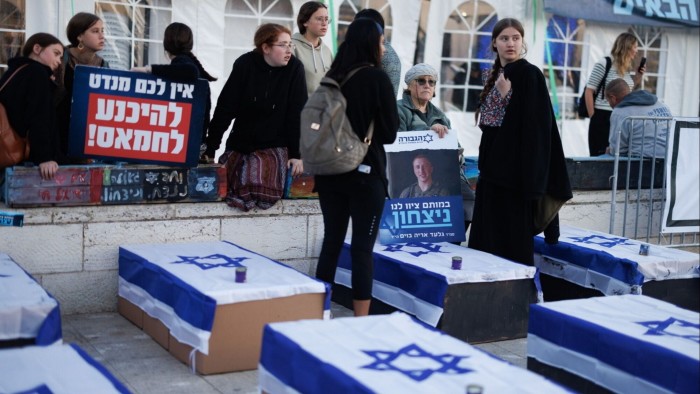 Protesters gather near coffin-like boxes draped with Israeli flags, holding placards in a demonstration against the ceasefire deal between Israel and Hamas