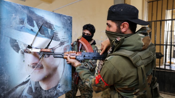 A fighter affiliated with Syria’s new administration bayonets a portrait of toppled president Bashar al-Assad at the defunct Mezzeh military prison in Damascus