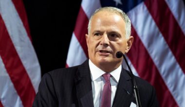 Ken Weinstein steht vor einer amerikanischen Flagge am Pult und spricht in ein Mikrofon