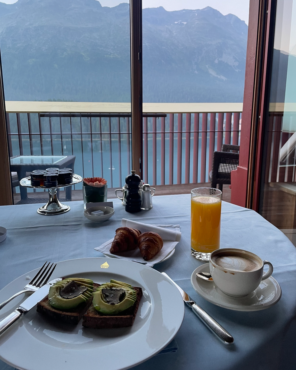 breakfast setting with avocado toast croissants coffee and orange juice overlooking mountains