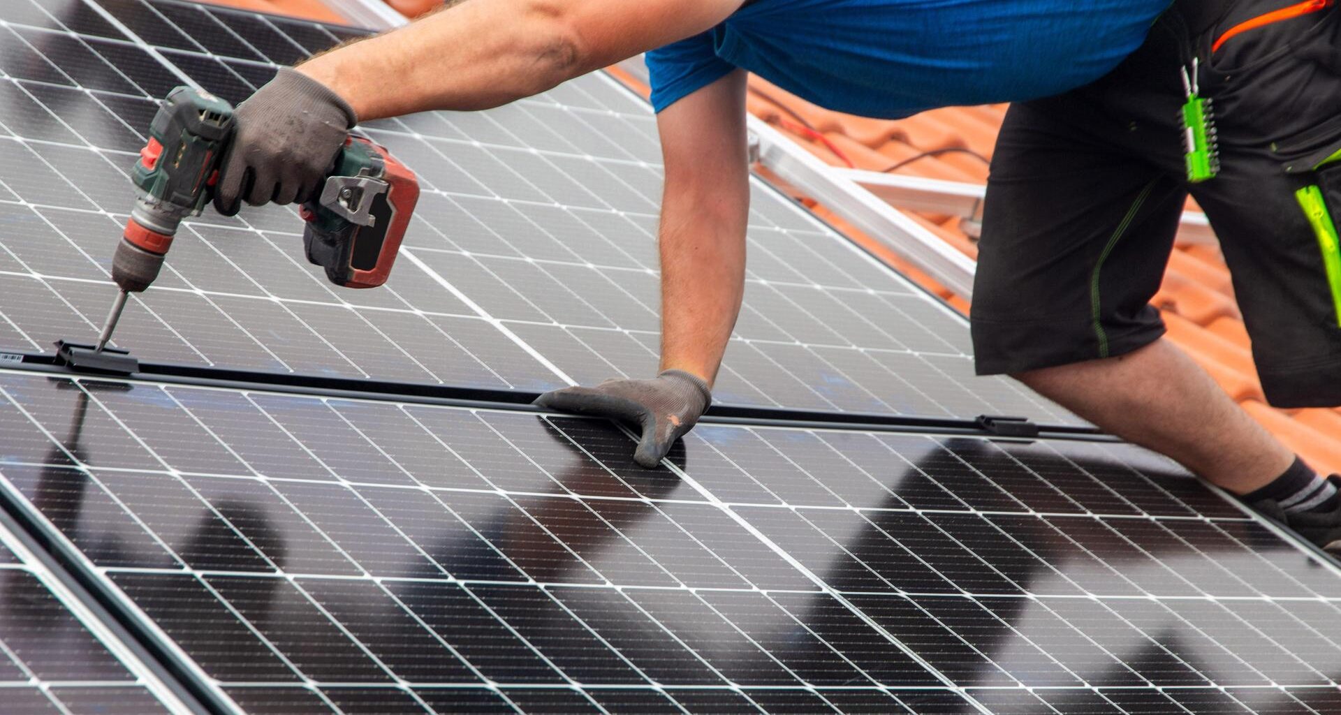 Ein Handwerker montiert eine Photovoltaikanlage auf dem Dach eines Einfamilienhauses.