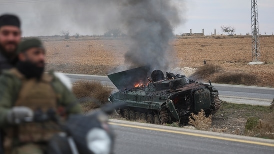 Syrian opposition fighters drive past a burning government armoured vehicle south of Hama, Syria, on Dec. 7, 2024. (AP)
