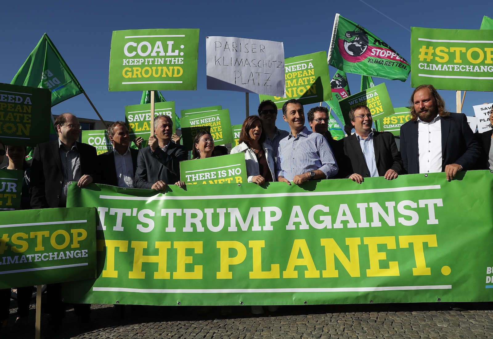 Protesters hold signs and a green banner reading "It's Trump against the planet"