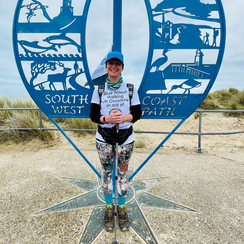 sign marking the south west coast path with a person in front holding a walking stick