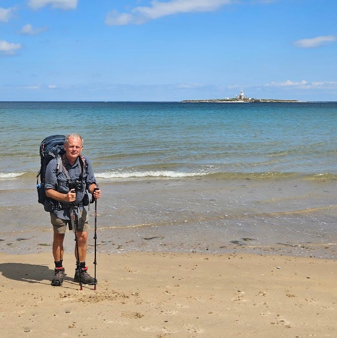 a hiker stands on a sandy beach with a backpack and trekking poles