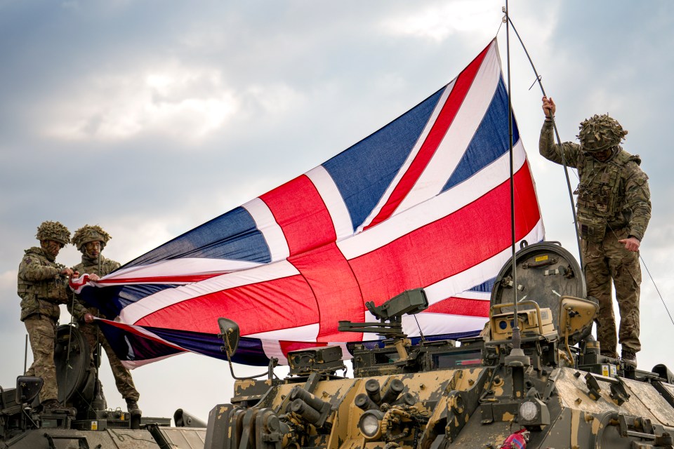 British soldiers raising the Union Jack flag on a military vehicle.