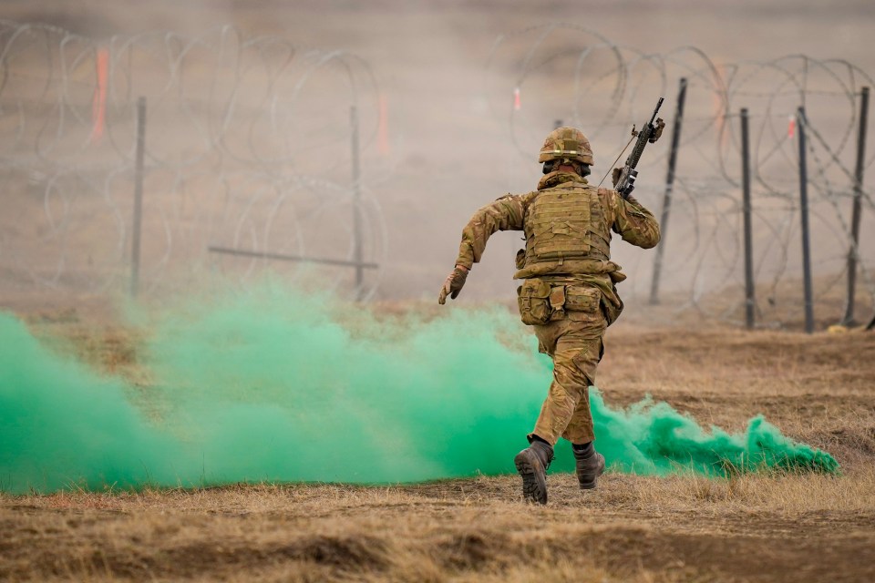 A soldier runs through green smoke during a NATO military exercise.