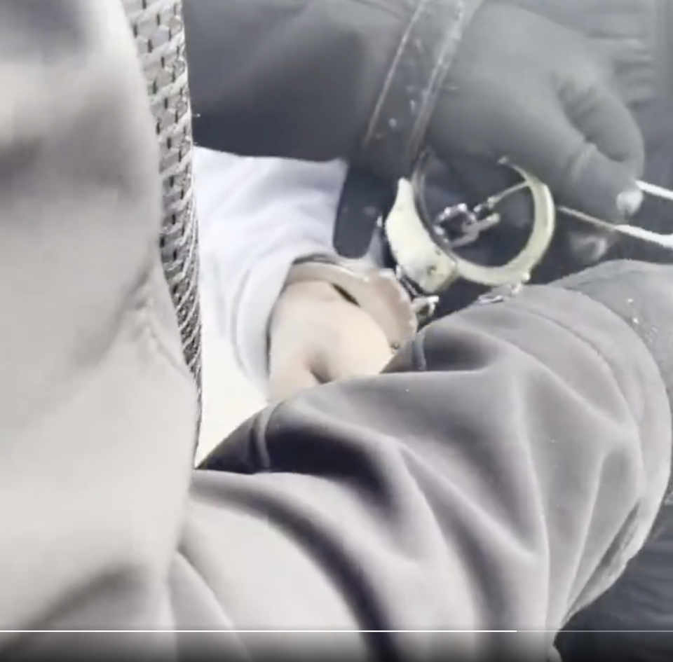 Close-up of a person in handcuffs, with hands held by someone wearing gloves