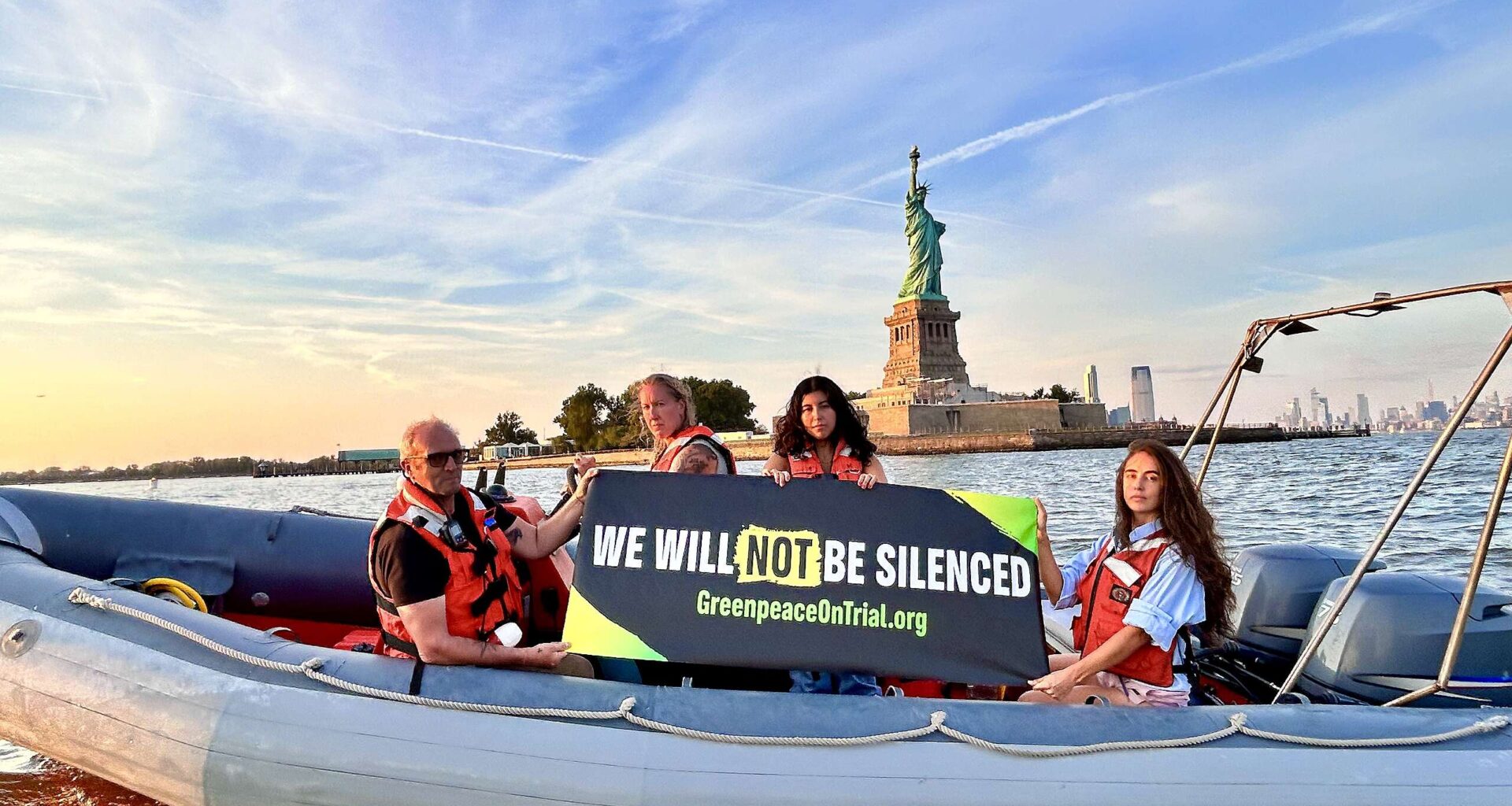Greenpeace activists on a boat in NYC in front of the Statue of Liberty holding a banner that says "We Will Not Be Silenced"