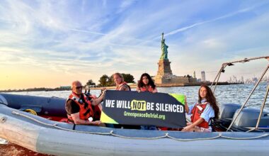 Greenpeace activists on a boat in NYC in front of the Statue of Liberty holding a banner that says "We Will Not Be Silenced"