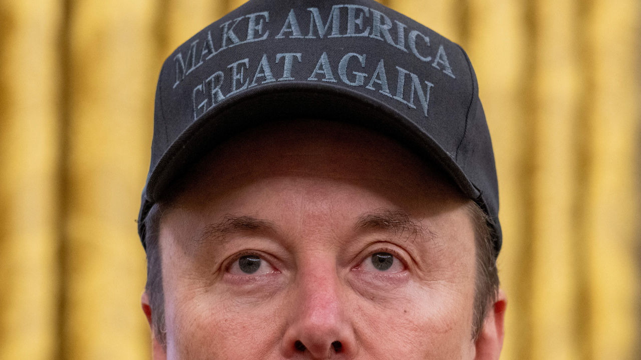 A close up shot of Elon Musks faces whilst wearing a black cap detailed with 'Make America Great Again'.