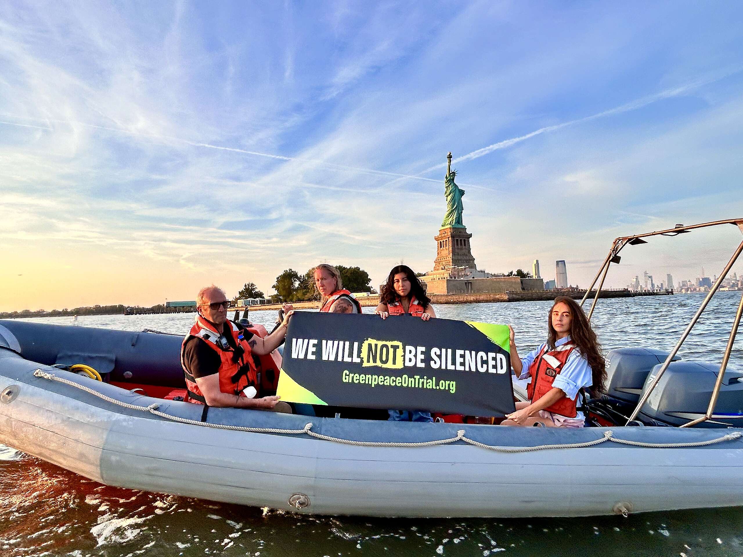 Greenpeace activists on a boat in NYC in front of the Statue of Liberty holding a banner that says "We Will Not Be Silenced"