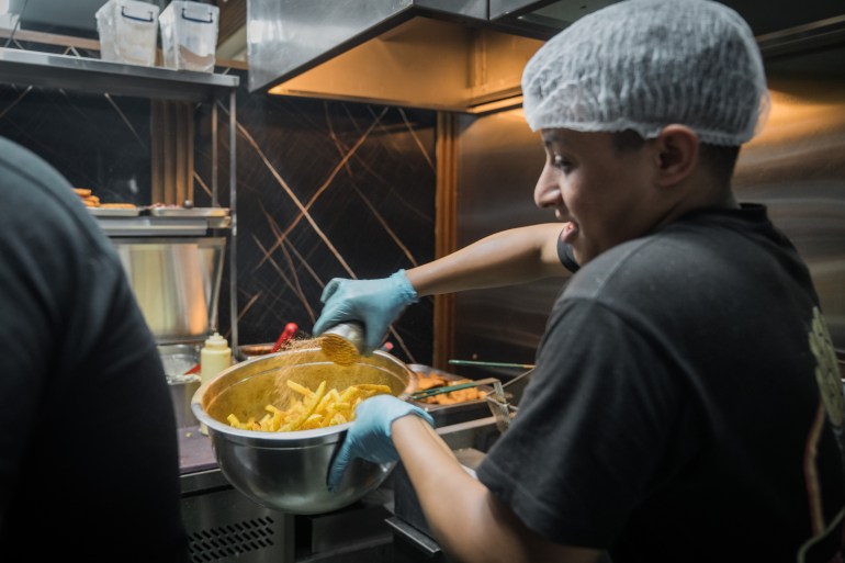 An employee at Fries Lab seasons french fries. [Raghed Waked/ Al Jazeera]