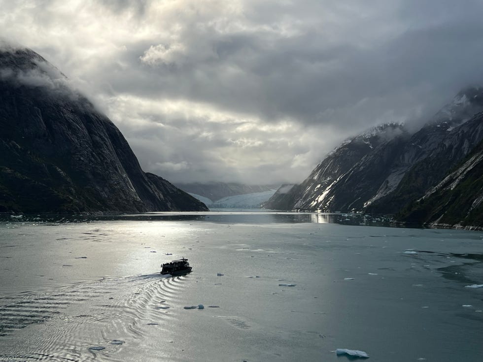 An excursion boat heads toward Dawes Glacier in Alaska, as passengers aboard the Celebrity Edge enjoy views from a distance.