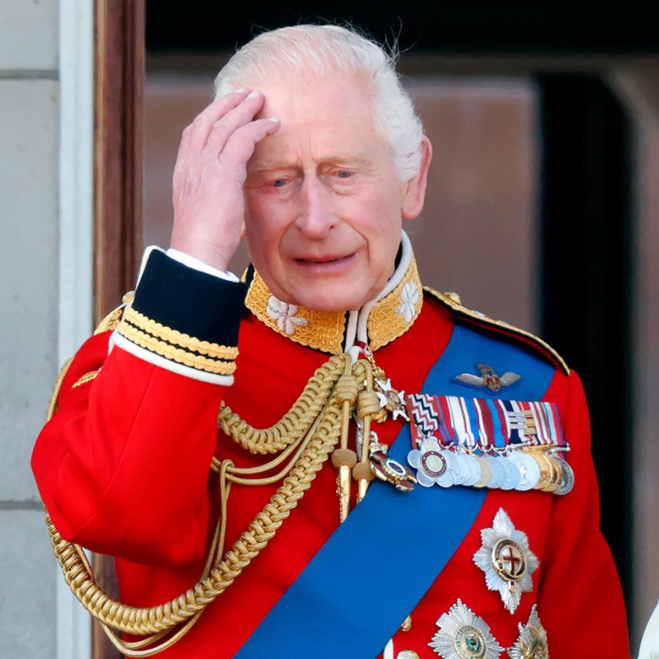 King Charles looks sad and holds his head while wearing a red military uniform.