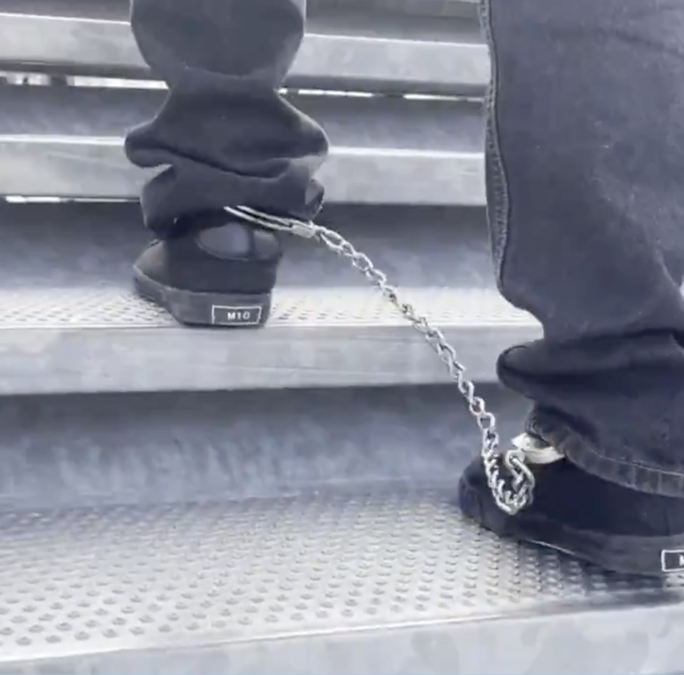 Person wearing chained shoes walks up metal stairs