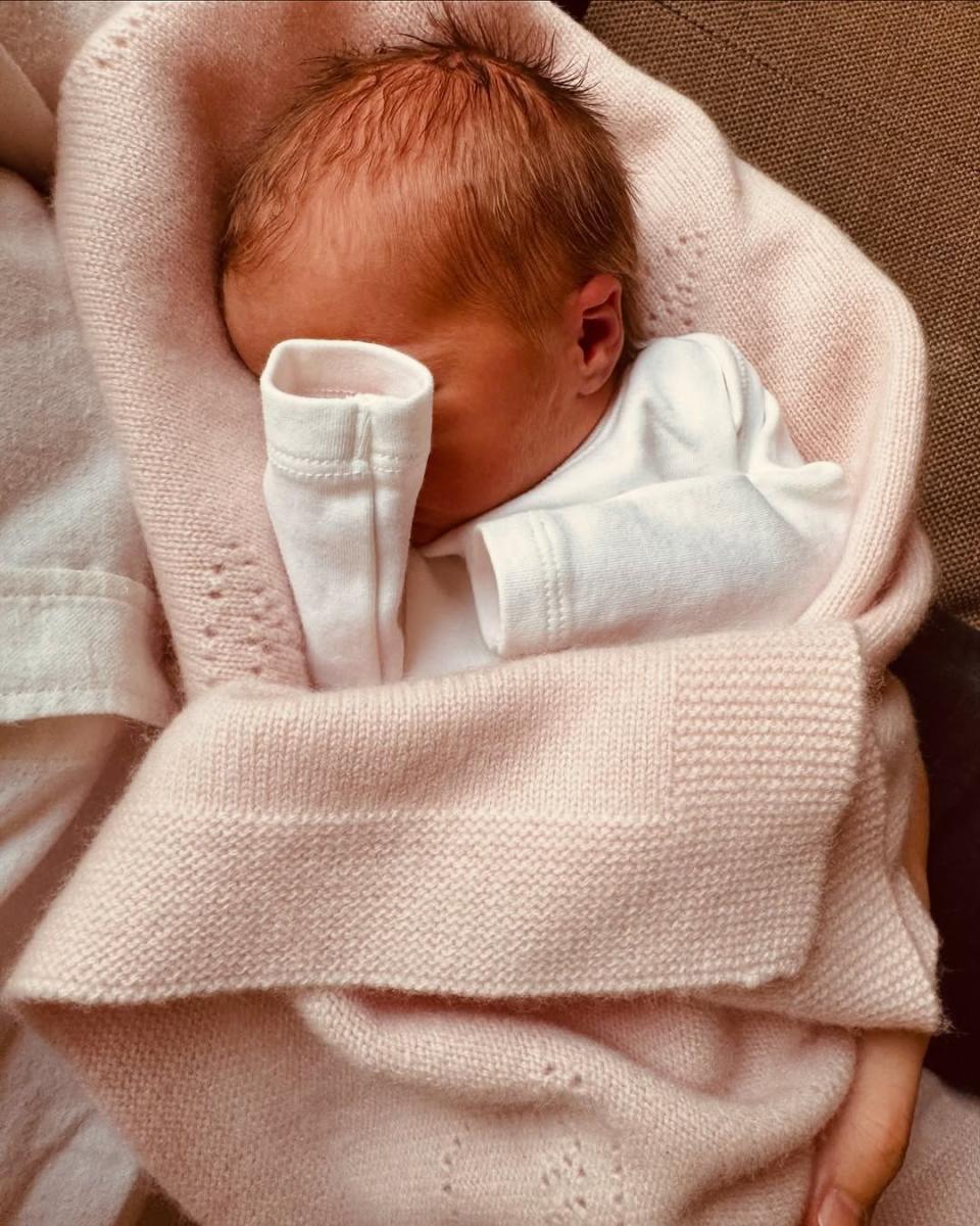 An infant wrapped in a soft pink blanket, held gently