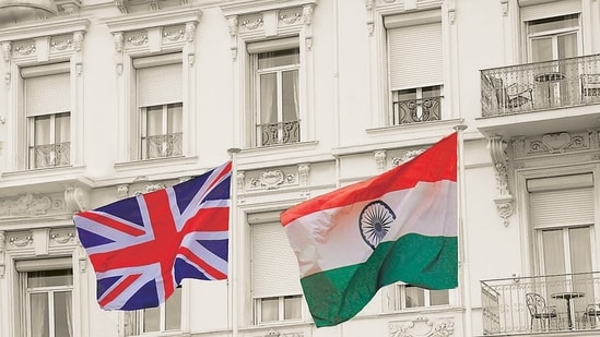 UK Great Britain and India national flag waving in the wind from flagpoles in front of a white mansion. (Shutterstock)