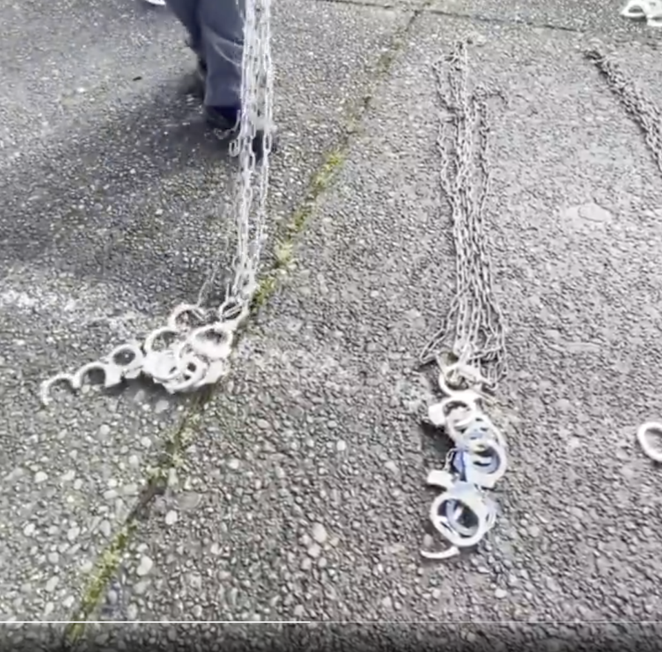 A person walks, dragging long chains and handcuffs along a textured pavement